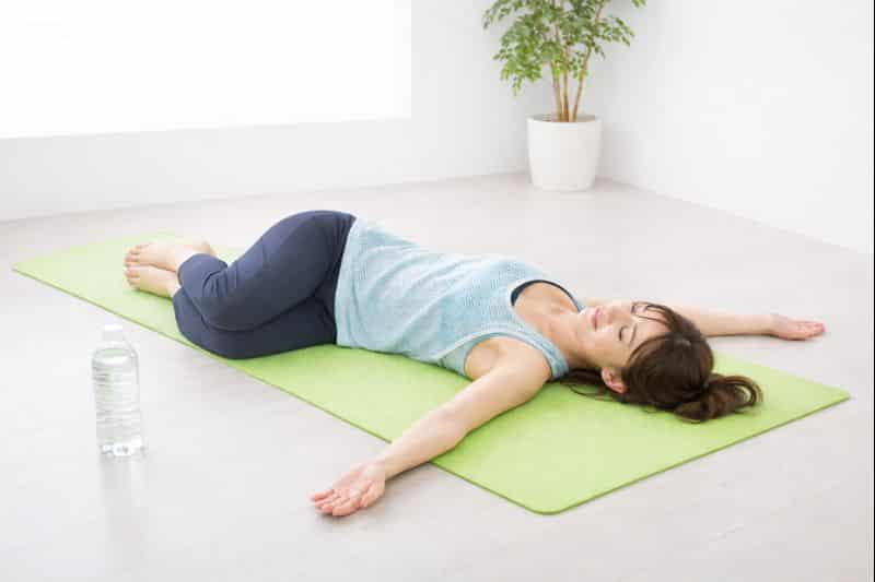 仰向けで膝を左右に倒し、雪かき後の腰や骨盤まわりをゆるめるストレッチを行う女性
