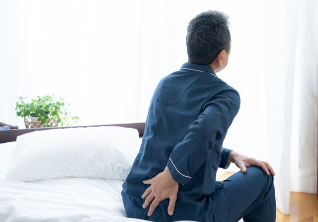 朝起きると腰が痛くて起き上がる男性のイメージ写真