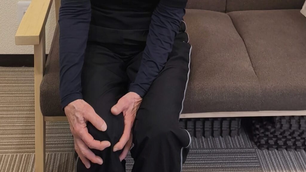 ソファに座り、ひざに手を当てているシニア女性