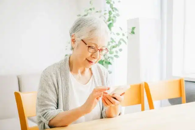 自宅でスマートフォンを見ながら情報を確認する高齢女性