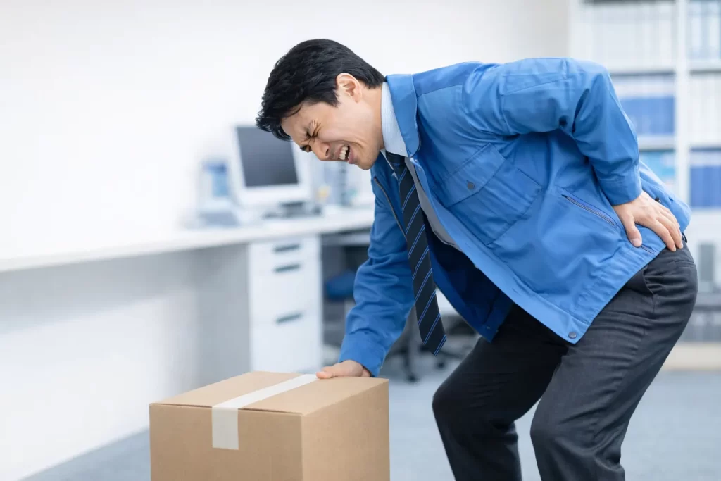 前かがみで段ボールを持ち上げようとして腰を痛めた男性
